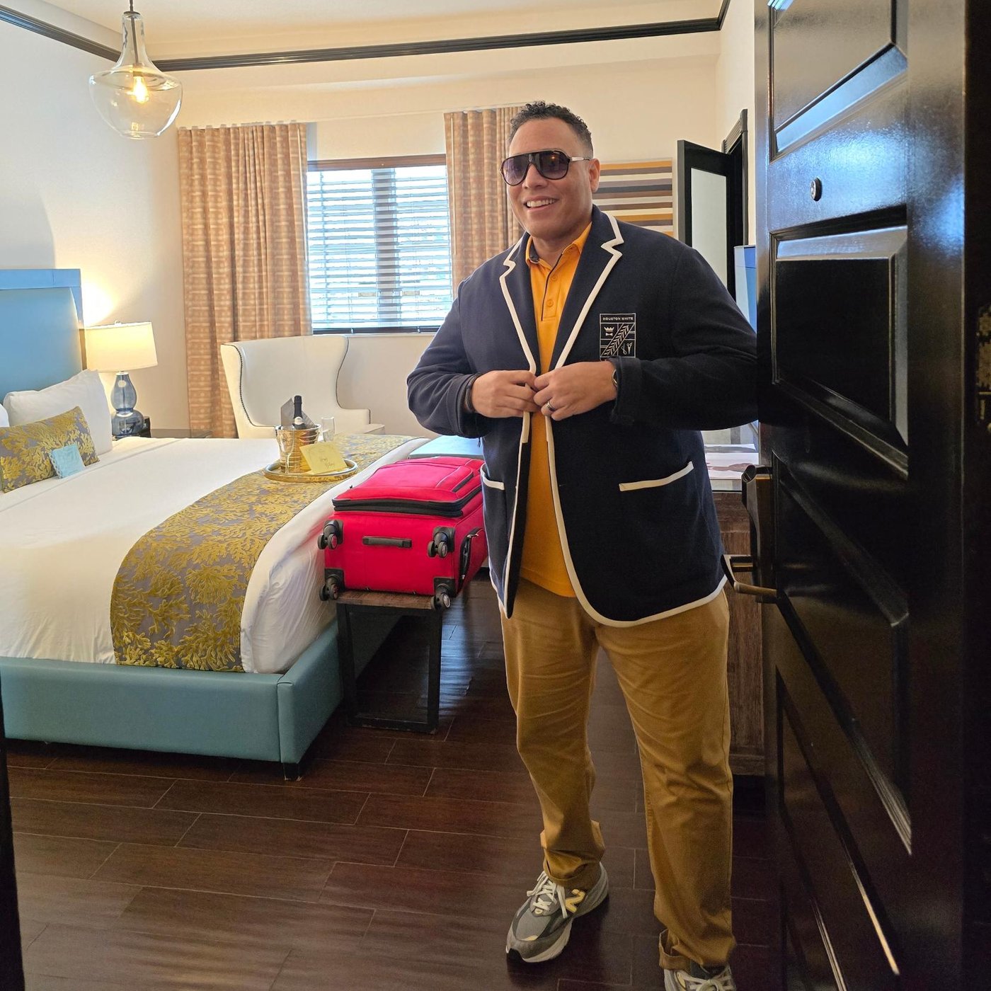 Nick in a hotel room in a navy blazer with a red suitcase